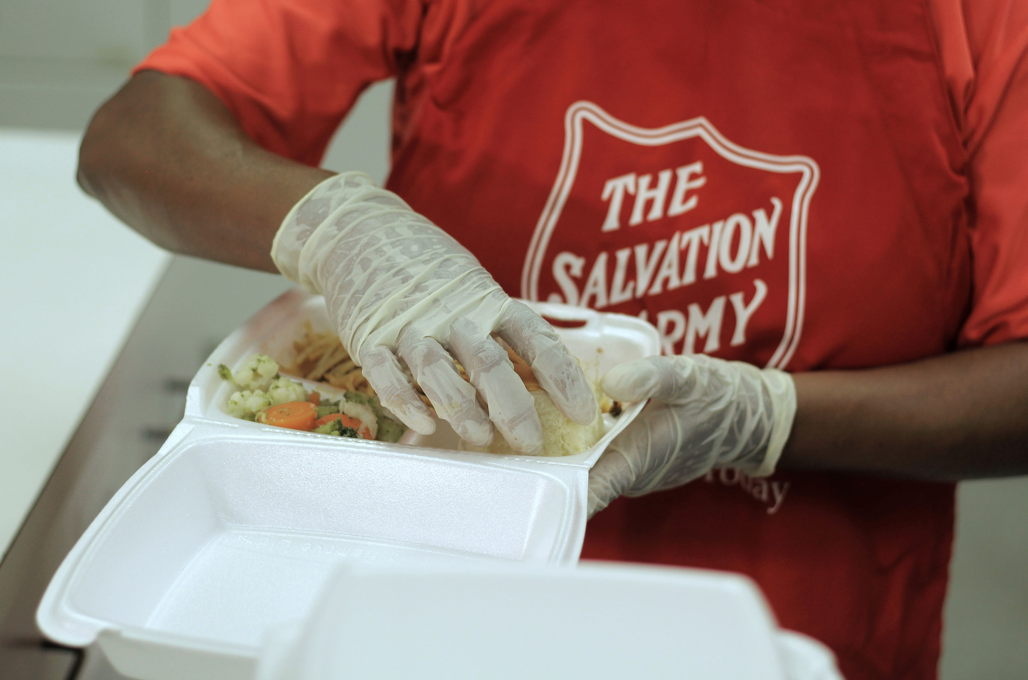 Salvation Army volunteer wearing gloves prepares a meal in a takeout container.